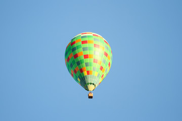 Green hot air balloon flying over the small city in a clear blue sky.