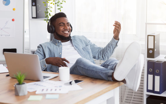 Black worker listening music in office and playing virtual guitar