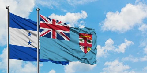Honduras and Fiji flag waving in the wind against white cloudy blue sky together. Diplomacy...