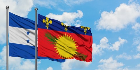 Honduras and Guadeloupe flag waving in the wind against white cloudy blue sky together. Diplomacy...