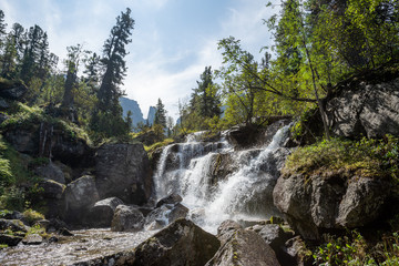 Naklejka premium Alpine waterfall in mountain forest under blue sky.