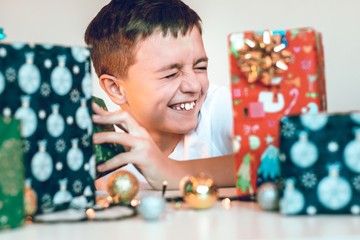 Fototapeta premium Young boy preparing gifts for the Christmas. Unpacking presents on the table. Winter holidays celebrating concept.