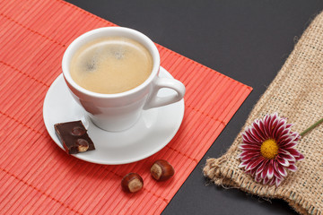 Cup of coffee with chocolate bar on bamboo napkin.
