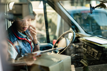 African American courier communicating on mobile phone while sitting in delivery van. - obrazy, fototapety, plakaty