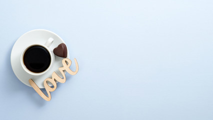 Top view coffee cup espresso with heart shaped chocolate candy and wooden word sign "Love" on blue background. Flat lay, overhead. Valentine's day concept.