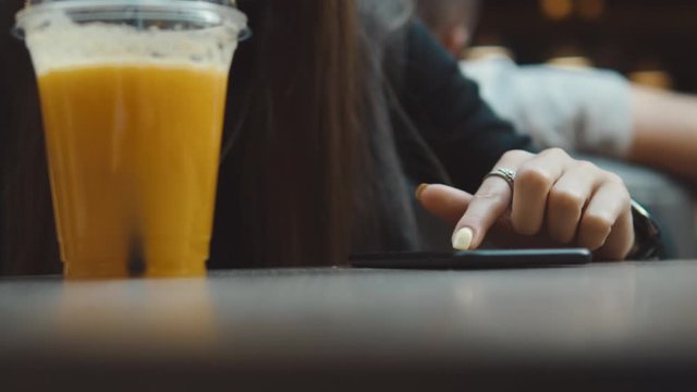 Young woman browsing on smartphone in cafe on wooden table, drinking juce. Businesswoman typing on mobile phone. 4K UHD