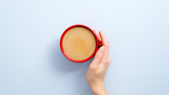 Female Hand Holding Latte Coffee Cup On Blue Background. Flat Lay, Top View, Overhead.