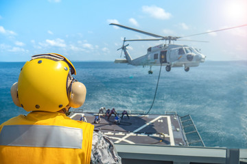 signal man give signal hand to a military navy helicopter above aviation deck on the ocean.  