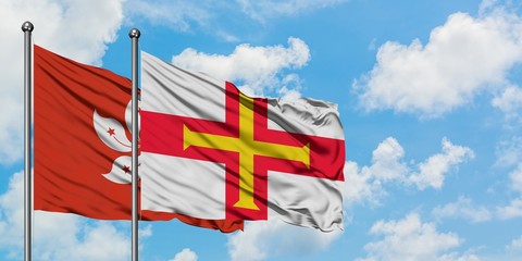 Hong Kong and Guernsey flag waving in the wind against white cloudy blue sky together. Diplomacy concept, international relations.