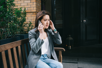 Thoughtful female speaking on mobile and resting on bench