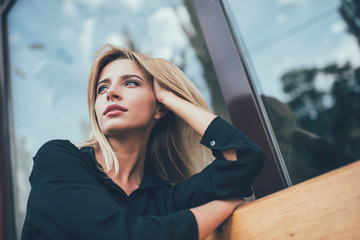 Fototapeta na wymiar Below view of pondering woman dressed in stylish black shirt thougthful looking away and thinking on ideas, attractive hipster girl in casual clothing lost in thoughts during rest time on city bench