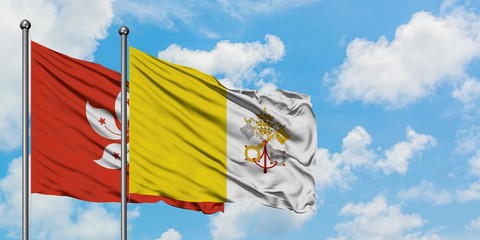Hong Kong and Vatican City flag waving in the wind against white cloudy blue sky together....