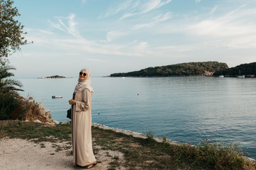 Fototapeta na wymiar portrait of young European Muslim women with hijab and looking at the camera. Sea is in the background. She is happy and relaxed.