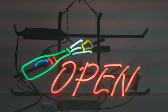 Open sign and bottle icon hanging on concrete wall in restaurant or alcohol store