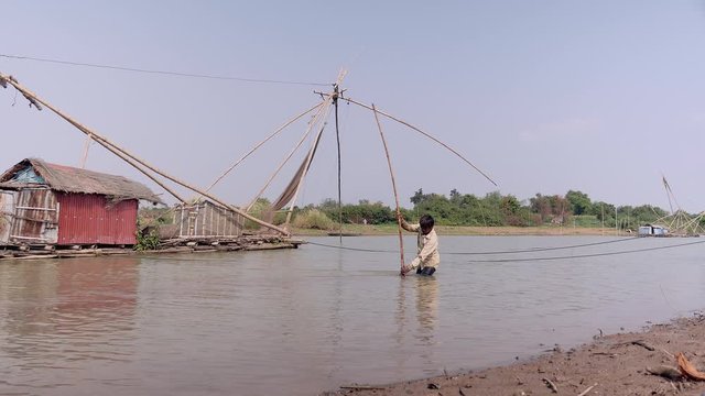 Clammer is digging for clams into the river-bottom by the riverside. Chinese fishing net  as backdrop