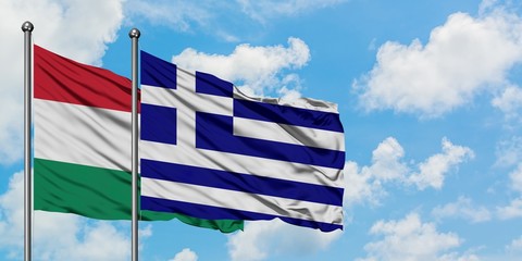 Hungary and Greece flag waving in the wind against white cloudy blue sky together. Diplomacy...