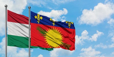 Hungary and Guadeloupe flag waving in the wind against white cloudy blue sky together. Diplomacy...