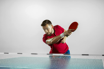 Possibility. Young man plays table tennis on white studio background. Model plays ping pong. Concept of leisure activity, sport, human emotions in gameplay, healthy lifestyle, motion, action, movement - obrazy, fototapety, plakaty