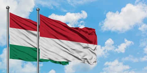 Hungary and Indonesia flag waving in the wind against white cloudy blue sky together. Diplomacy...