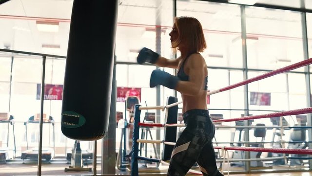 Boxer girl. Young kickboxing woman training punching bag in fitness club