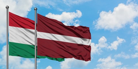Hungary and Latvia flag waving in the wind against white cloudy blue sky together. Diplomacy concept, international relations.