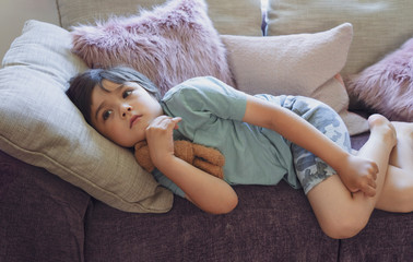 Protrait of happy boy lying on fluffy pillow on sofa, Selective focus Adorable child watching TV and relaxing at home on weekend, Warm and cozy scene in Pastel tone