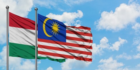 Hungary and Malaysia flag waving in the wind against white cloudy blue sky together. Diplomacy concept, international relations.