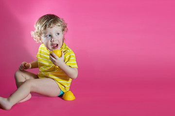 Cute little boy in yellow jacket with lemon in hand, pink wall on background. Close up studio portrait of boy.