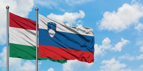 Hungary and Slovenia flag waving in the wind against white cloudy blue sky together. Diplomacy...