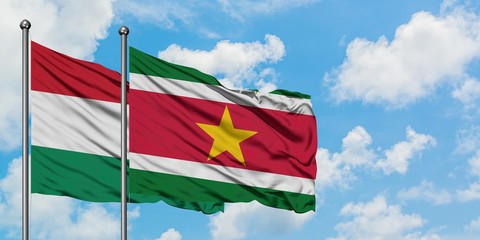 Hungary and Suriname flag waving in the wind against white cloudy blue sky together. Diplomacy...