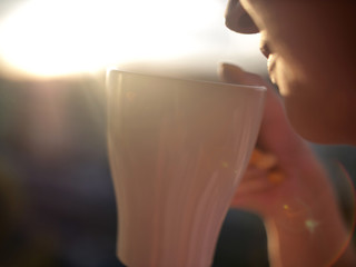 White mug in the hands of a young woman on a sunset background, close-up