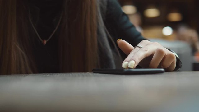 Young woman browsing on smartphone in cafe on wooden table, drinking juce. Businesswoman typing on mobile phone. 4K UHD