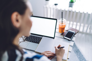 Anonymous woman working with laptop and writing notes