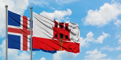Iceland and Gibraltar flag waving in the wind against white cloudy blue sky together. Diplomacy...