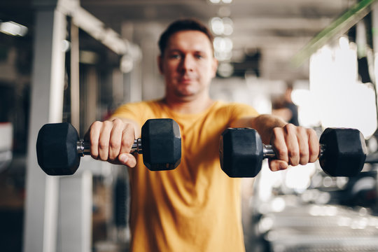 authentic image, fit coach man lifting weight, training bicep curl in the gym. concept of weight loss and healthy living. selective focus - focus is on the dumbbells.