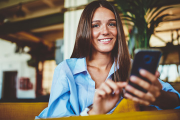 Portrait of happy cheerful hipster girl smiling and looking at camera while holding smartphone...