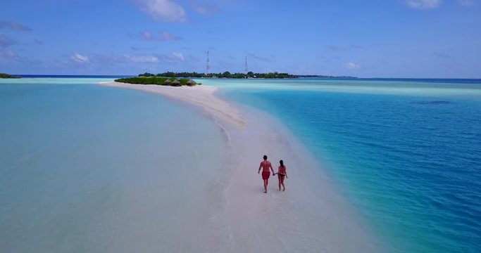 Hand-held couple talking about their relationship and vacation days walking on narrow sandy stripe across turquoise lagoon in Bermuda