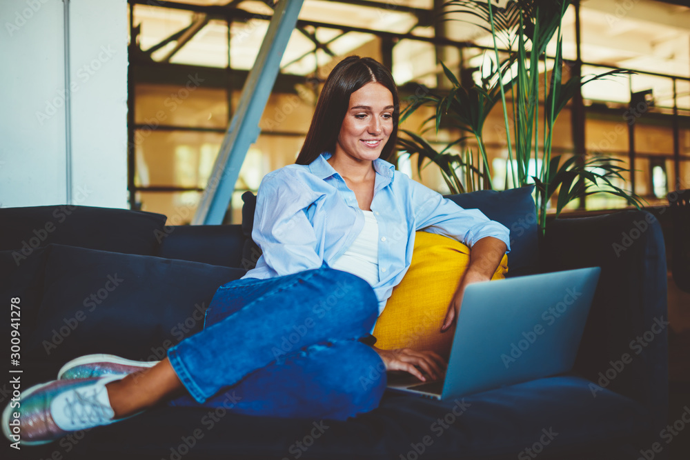 Poster positive smiling hipster girl searching comedy show for watching using modern laptop device indoors,