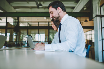 Young smart bearded male entrepreneur writing down to notepad general concepts of business startup.Creative male and female marketing experts developing together new advertising campaign in office