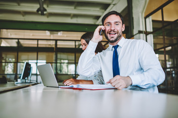 Obraz premium Half length portrait of positive hipster guy communicating with chief in funny atmosphere and emotionally reacting to getting new position.Cheerful male employee looking at camera during phone talk