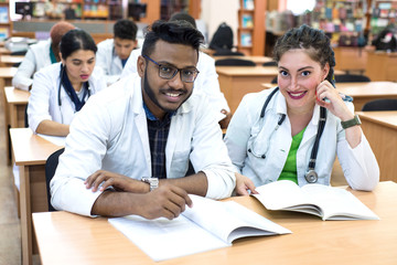 a group of young medical students of mixed race. Sitting at the table, looking at the camera, smiling