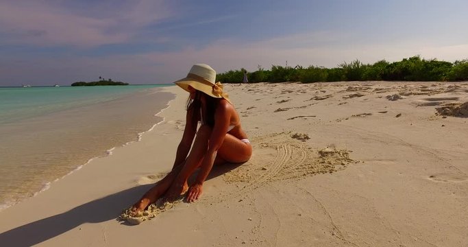 Beautiful girl with straw hat in white bikini playing with white sand of exotic beach in Jamaica
