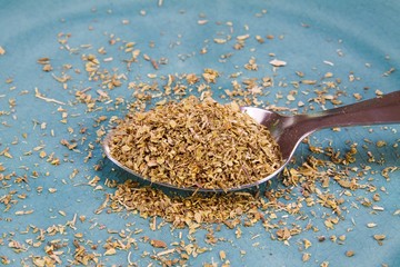 Close up of isolated spoon full with dry oregano herb spice on scratched old blue china dish