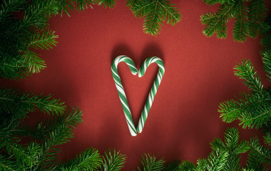 Christmas composition. Branches of spruce, lollipop cane in the shape of a heart on a red background. Christmas, winter, new year concept. Flat lay, top view, copy space