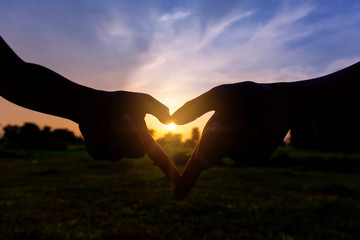 Silhouette hands of two child are symbolized as a heart shape on nature sunset - 300945437