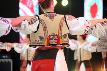 Dancers hold hands in a traditional Romanian dance wearing traditional beautiful costumes. - obrazy, fototapety, plakaty