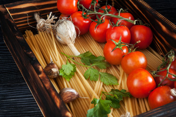 Raw pasta with cherry tomatoes garlic and parsley in wooden box