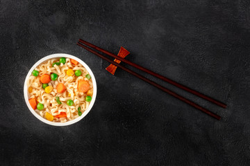 Fototapeta na wymiar Ramen cup, instant noodles in a plastic cup, top shot with chopsticks and a place for text on a dark black background