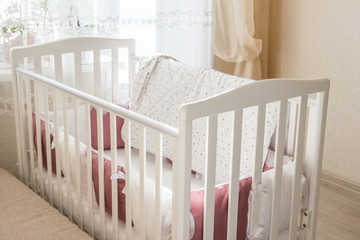 Fototapeta na wymiar Baby bed crib with white and Burgundy color pillows with laces