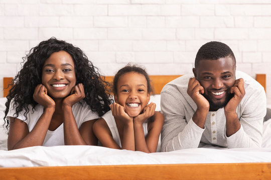 Portrait of happy black family lying on bed together